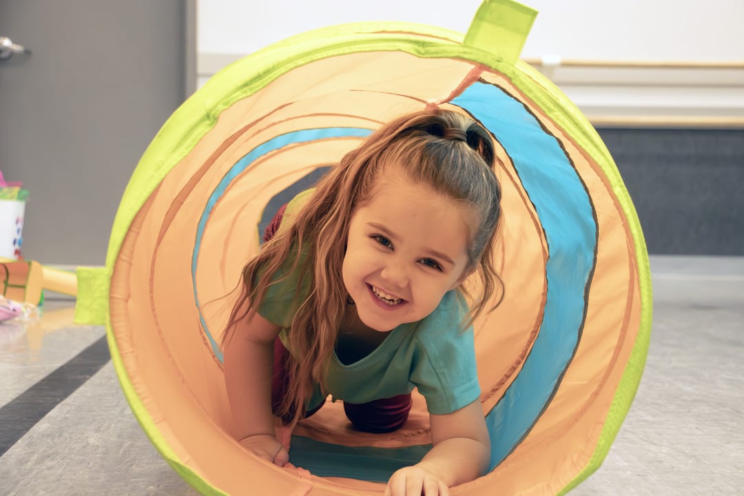 Young camper crawling through a colorful play tunnel at summer dance camp